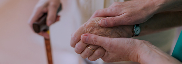 hands of a carer holding 1 hand of an elderly resident to help her walk