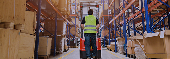 back of a man riding a fork lift through a warehouse