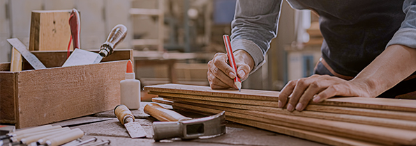 man in a workshop marking up pieces of wood to be cut